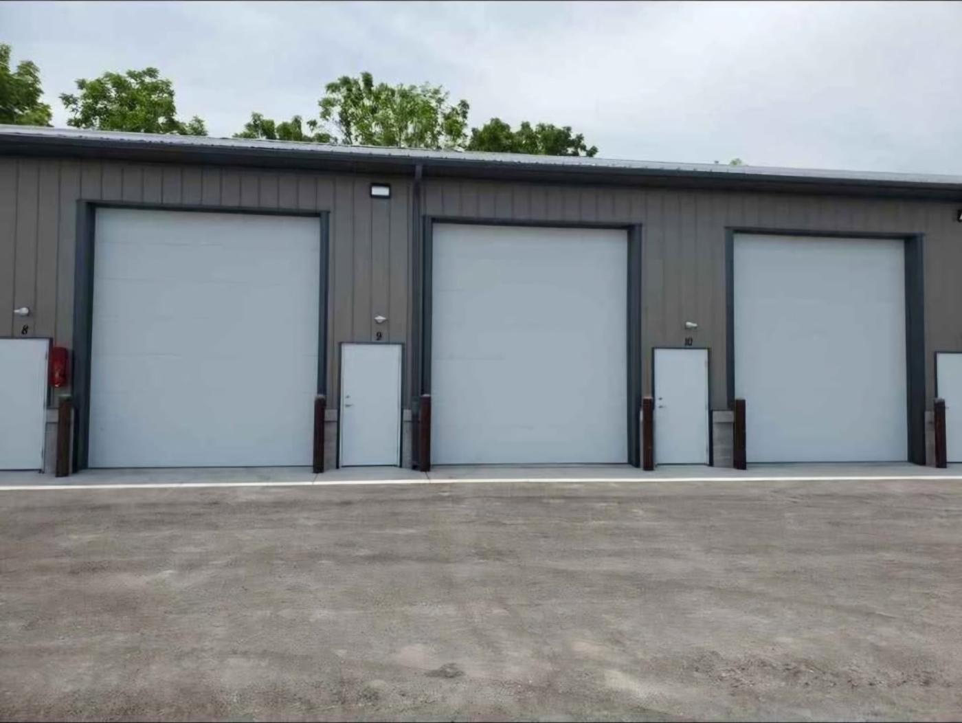 Three storage units with large overhead doors, numbered walk-in doors and protective bollards