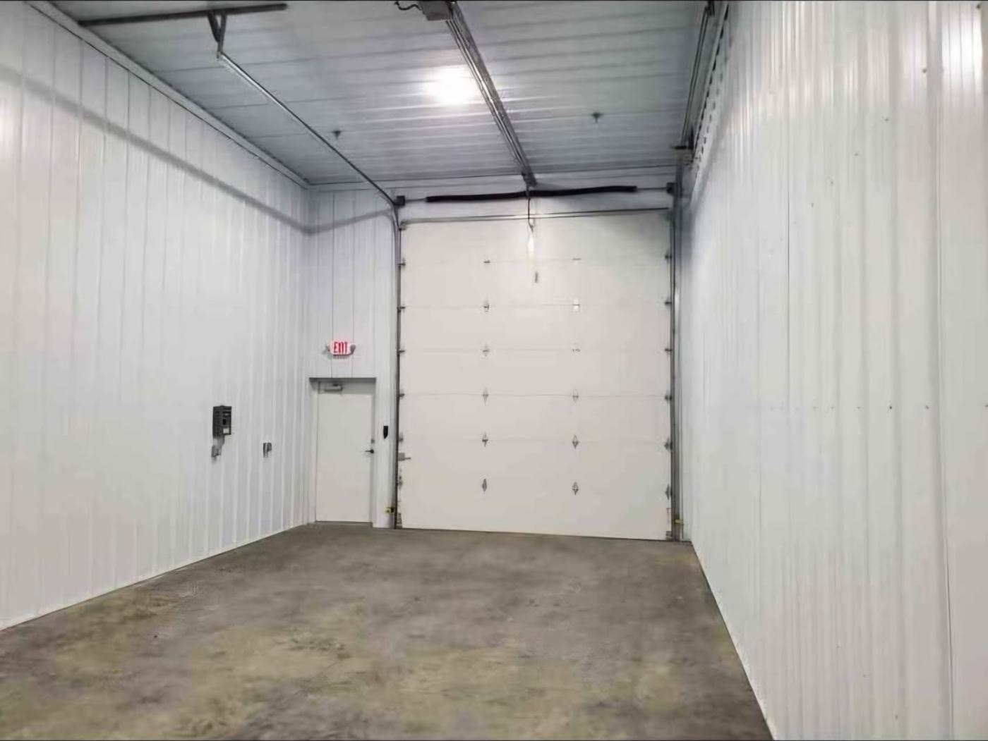 Inside a storage bay looking toward the tall overhead door and walk-in exit door