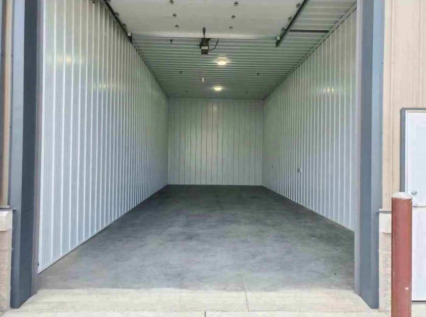 Interior of an empty storage bay seen through the open overhead door, with white steel walls and concrete floor
